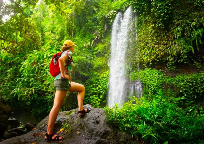 A young woman backpacker admiring a waterfall in the jungle.