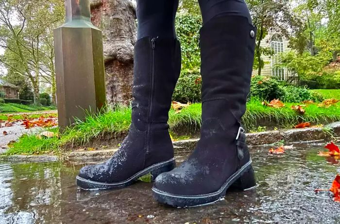 A person sports Overland Women's Major Shearling-Lined Waterproof Suede Boots outdoors in the rain