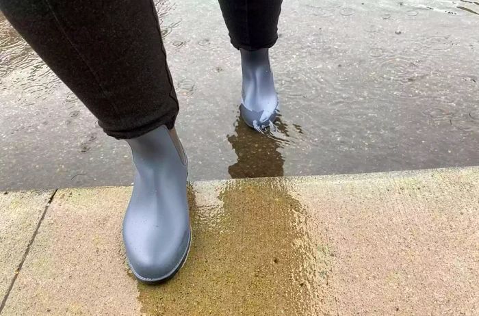 An individual wearing the Asgard Chelsea Ankle Waterproof Rain Boots walks through water