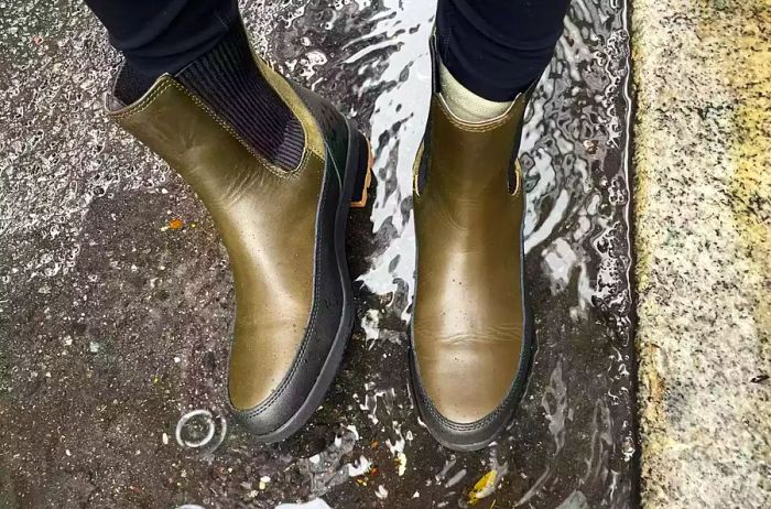 A person stands in water while donning Forsake Sofia Chelsea Women's Waterproof Outdoor Boots