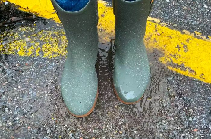 A close-up of feet in Bogs Women's Sweetpea Tall Rain Boots as they stand in the rain