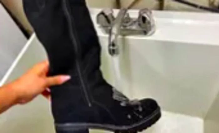 A hand grasps an Overland Women's Major Shearling-Lined Waterproof Suede Boot beneath a running faucet