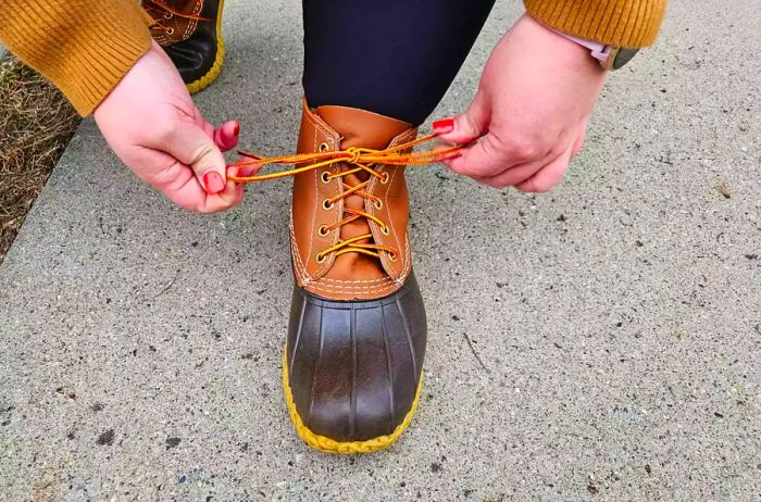 A person laces up a pair of L.L. Bean Women's 6-Inch Bean Boots