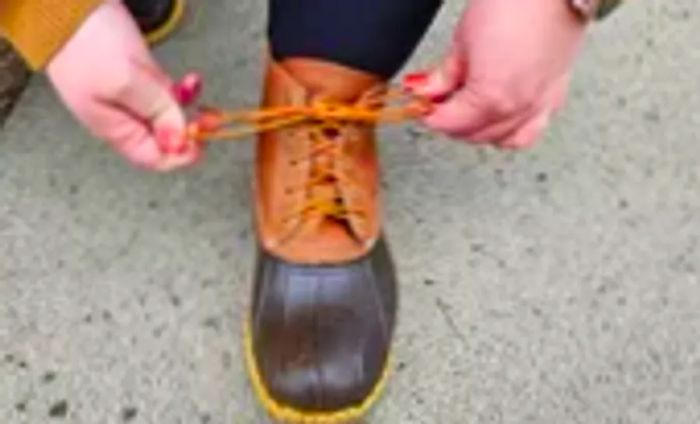 A person fastens the lace on a L.L. Bean Women's 6-Inch Bean Boot