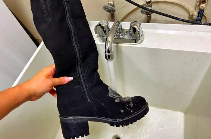 A hand demonstrates an Overland Women's Major Shearling-Lined Waterproof Suede Boot beneath a running faucet