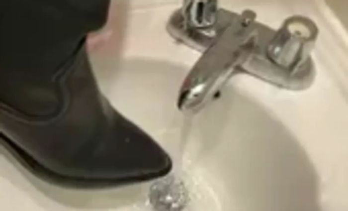 A person holds a La Canadienne Paton Leather Boot under a running faucet