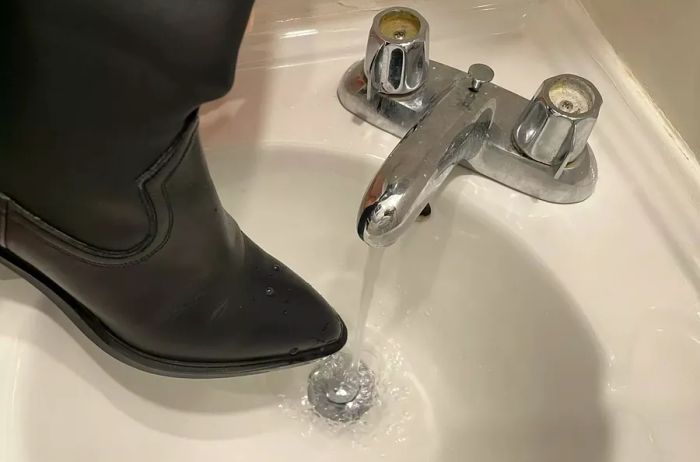 A person holds a La Canadienne Paton Leather Boot under running water