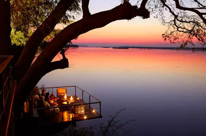 Guests relax on a deck with a view of the river at sunset