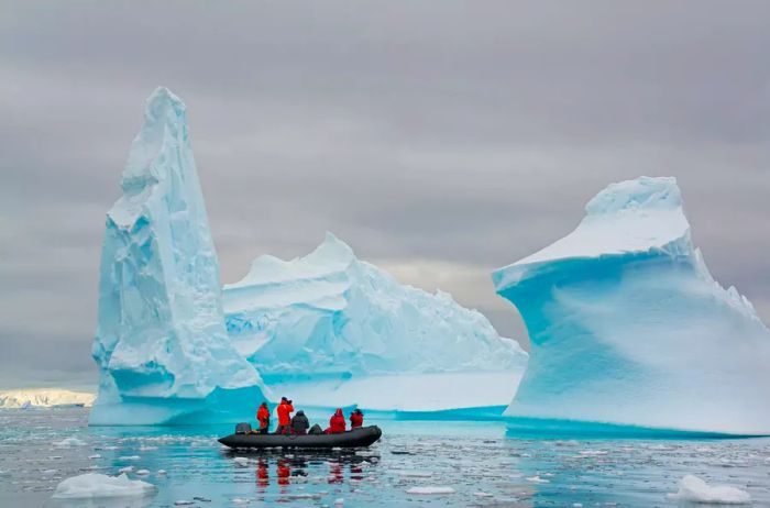 Groups in small inflatable Zodiac boats navigating past towering, sculpted icebergs in the tranquil waters surrounding the small islands of the Antarctic Peninsula.