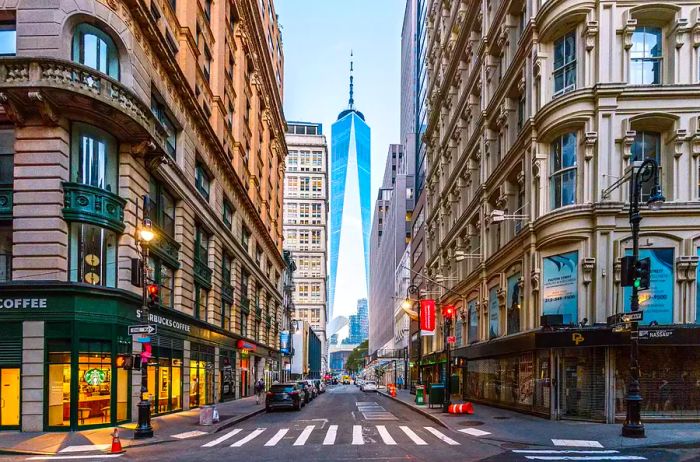 A bustling street in Downtown Manhattan with One World Trade Center prominently visible, New York City