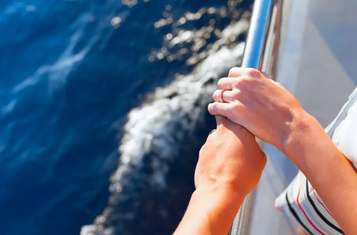 A close-up shot of a couple clasping hands at the edge of a cruise ship.