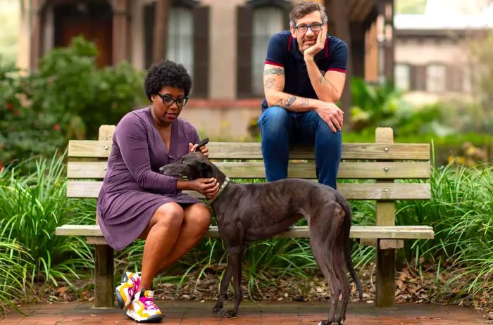 Outdoor portrait featuring Mashama Bailey and John O. Morisano with a dog seated on a bench