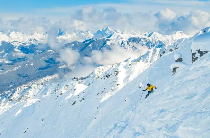 A skier gracefully descending a snow-covered mountain, framed by towering peaks in the background.