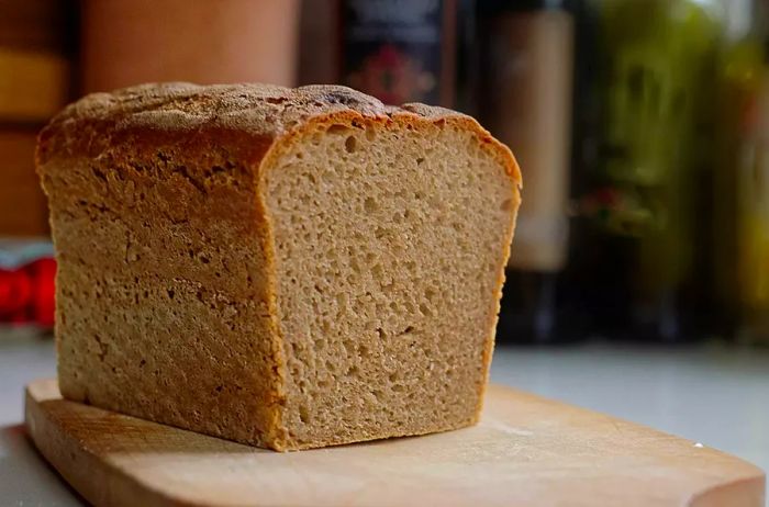 A freshly baked loaf of sourdough resting on a cutting board in a kitchen