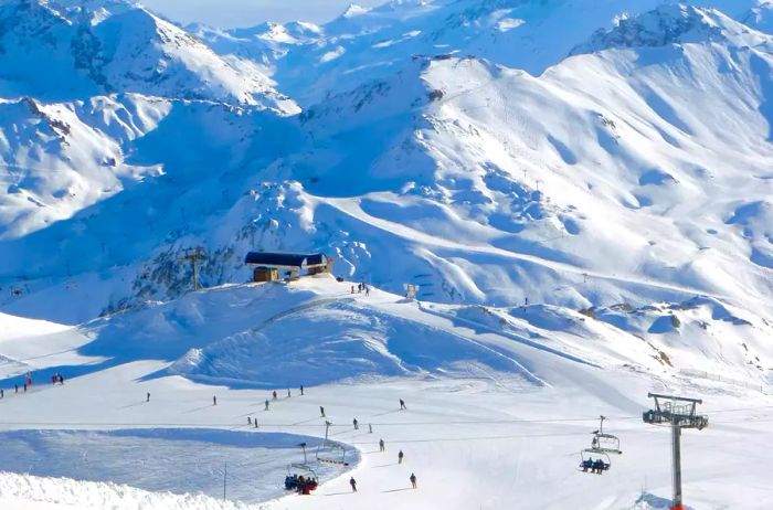 A valley and mountains in the French Alps featuring ski pistes with skiers and ski lifts.