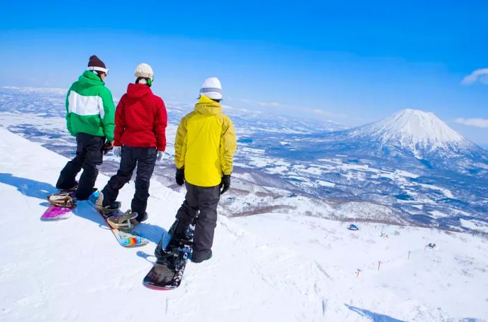 Three snowboarders perched on a slope, with a stunning view of Mt. Fuji in the background.