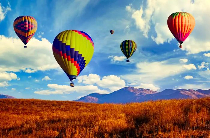 A stunning photograph captured at sunrise shows five vibrant hot air balloons soaring over Temecula, California, each adorned with a variety of bright colors.