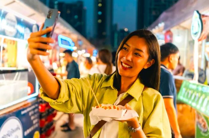 An Asian woman delights in savoring fries from a street food stall at a night market