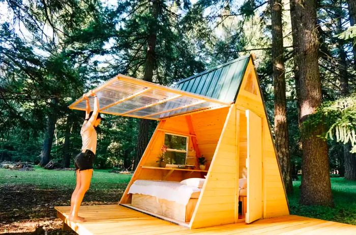 A woman lifting the window of an A-Frame cabin.