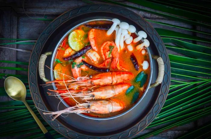 A vibrant bowl of Tom Yum Goong, a spicy Thai shrimp soup enriched with lemongrass, lime, galangal, and topped with chilies, captured from a top view against a dark backdrop.