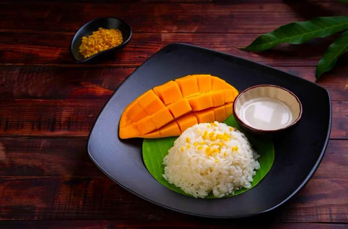 A delightful serving of Thai sweet sticky rice paired with ripe mango on a black plate, known as Khao Niew Ma Muang.