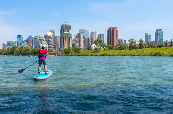 Images and videos showcasing creativity: A woman paddleboarding with Calgary’s skyline as a backdrop.