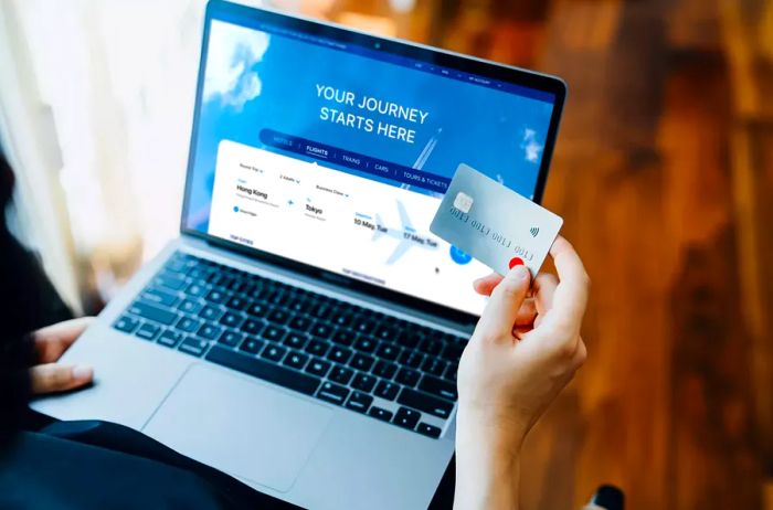 Close-up of a young woman booking airline tickets online using her laptop, entering credit card information to finalize the payment at home. Travel planning. Organizing a vacation online. Travel and business trip planning - stock photo