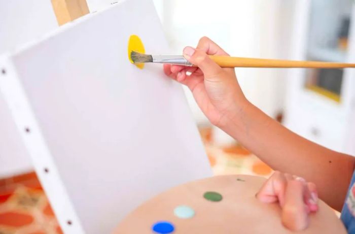 Close-up of a boy's hands painting on a canvas while holding a palette. A concept centered on art and hobbies.