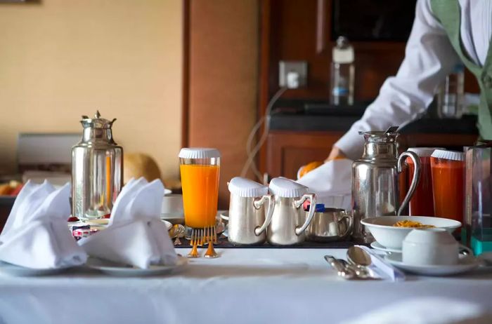 A breakfast spread in a hotel room featuring fruits, juices, coffee, and tea