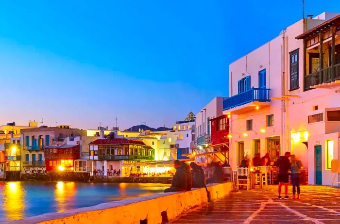 Experience the vibrant Little Venice district in Mykonos, where bars and restaurants line the seaside, creating a picturesque setting at dusk in Greece. The Greek resort comes alive at night.