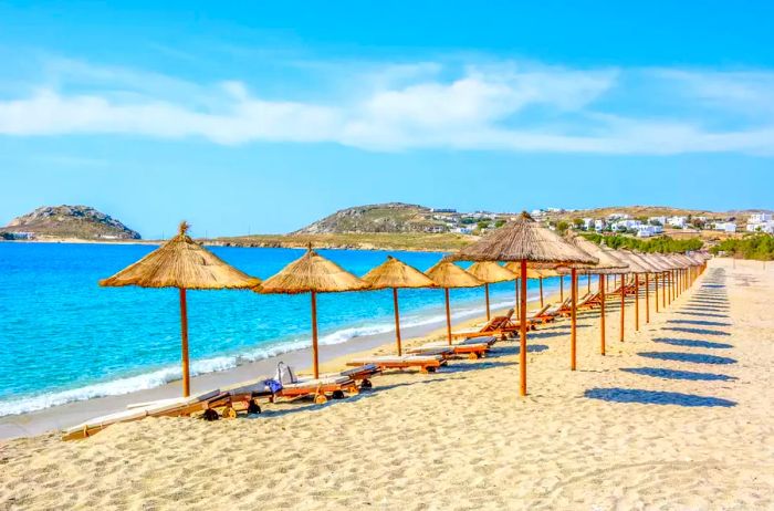 The sandy beach near the azure sea, adorned with sunbeds and umbrellas. Mykonos