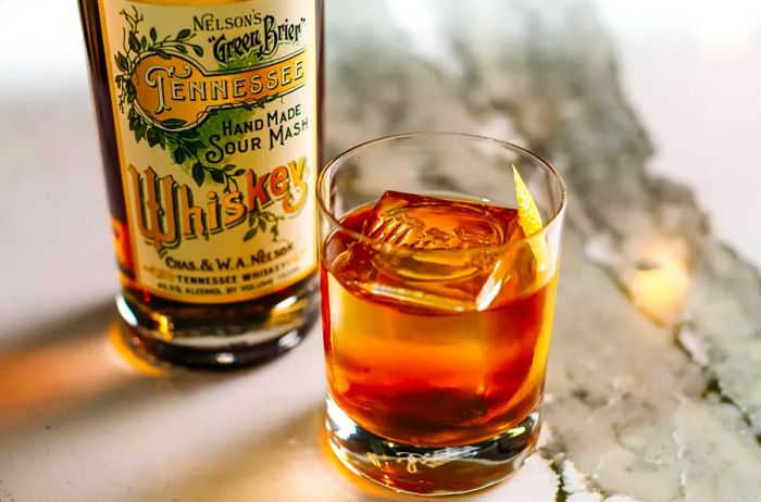 An old fashioned cocktail next to a bottle from Nelson's Green Brier