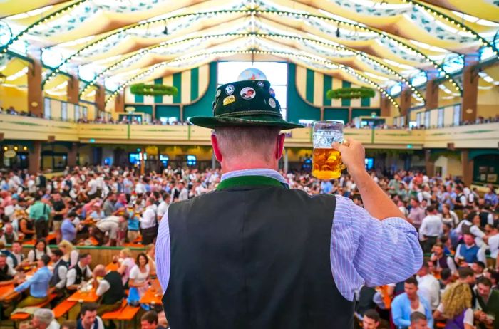 Man in lederhosen raising a beer in an Oktoberfest tent