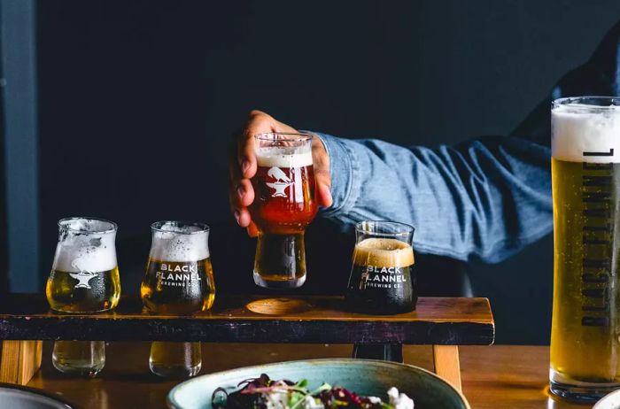 A hand presenting a glass from a tasting flight at Black Flannel Brewing