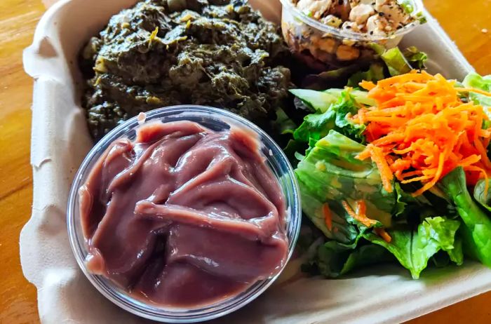 Hawaiian Lau Lau plate served with fresh or day-old poi in a bowl, salad, and tofu poke in a cardboard container on a table.