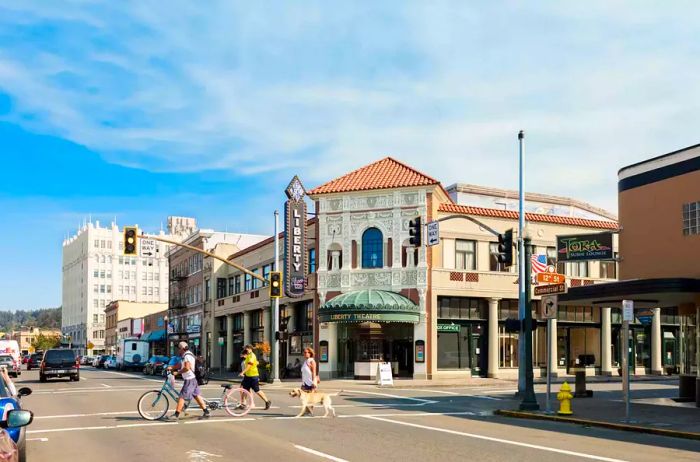 Pedestrians, cyclists, and a dog navigate an intersection in downtown Astoria, Oregon.