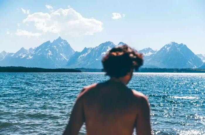 A person stands with their back to a breathtaking lake and mountain view