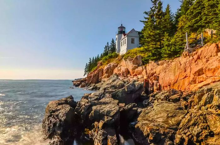 A breathtaking view from the rugged cliffs towards Bass Harbor Head Light, which was constructed in 1858 and stands on the Maine coast within Acadia National Park on Mount Desert Island.