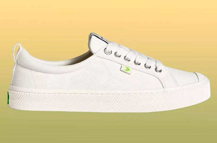 The Cariuma Oca Low sneaker displayed against a yellow to green gradient background