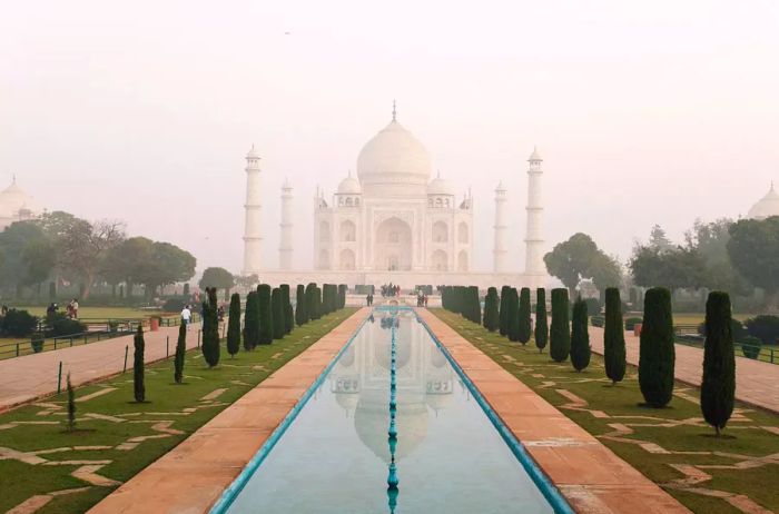 View of the long pool lined with trees in front of the Taj Mahal on a misty day