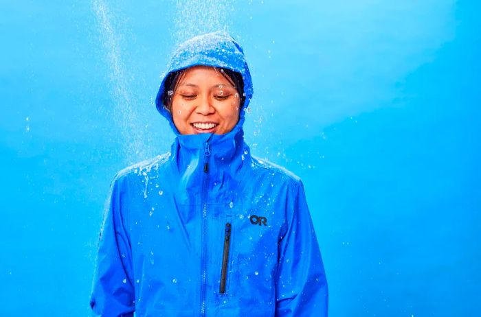 A person standing beneath a simulated shower while wearing the Outdoor Research Women's Aspire Super Stretch Jacket