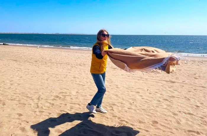 A person lays the Coyuchi Mediterranean Organic Towel on the beach.