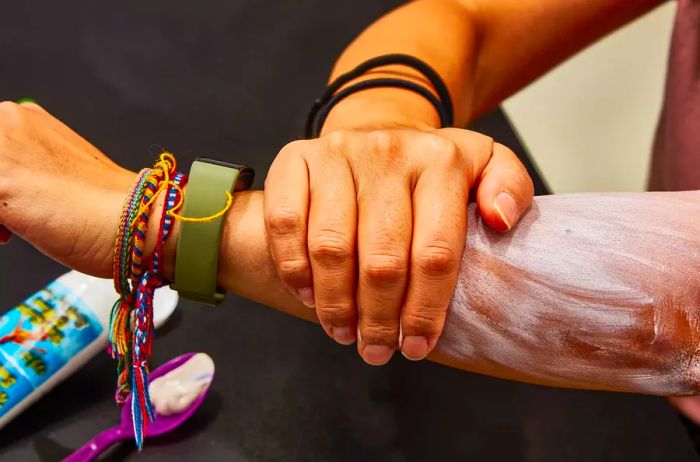 A hand applying Maui Surfer Honey All Natural Sunscreen on an arm against a dark backdrop