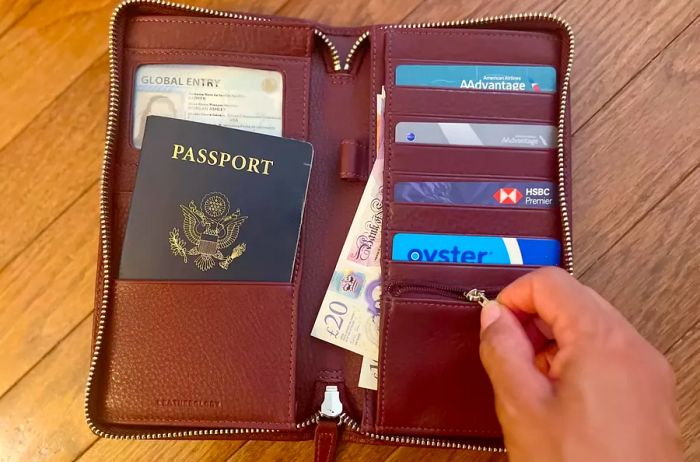 A person unzipping the coin compartment of the Leatherology Travel RFID Wallet, filled with cards and a passport.