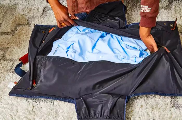 Hands zipping up the Mark & Graham Commuter 2-in-1 Garment Bag filled with clothing