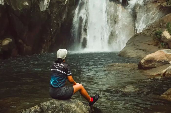 A woman relaxes next to a waterfall in Malaysia.