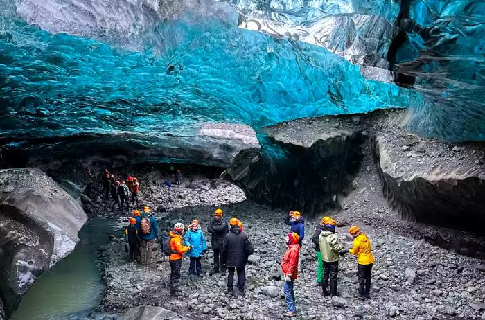 Individuals stand beneath a blue-hued frozen glacier inside a cave in Iceland