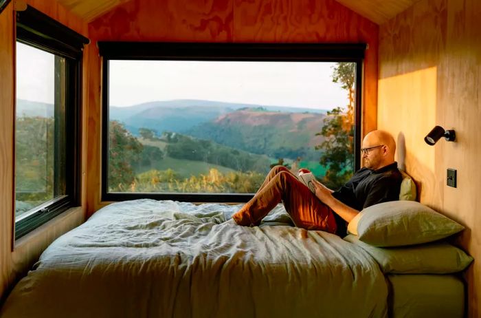 A man relaxes on a bed, engrossed in a book within a cabin