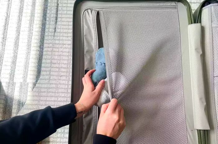 An individual placing socks into an internal compartment of the Monos Check-in Medium