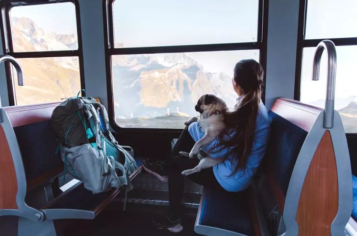 A woman backpacker and her dog enjoying a ride on the mountain train in the Swiss Alps.